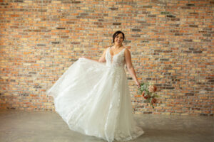 A bride to be modeling the Oaklyn, a dress with illusion front and back, a deep v neck and a chapel length train.