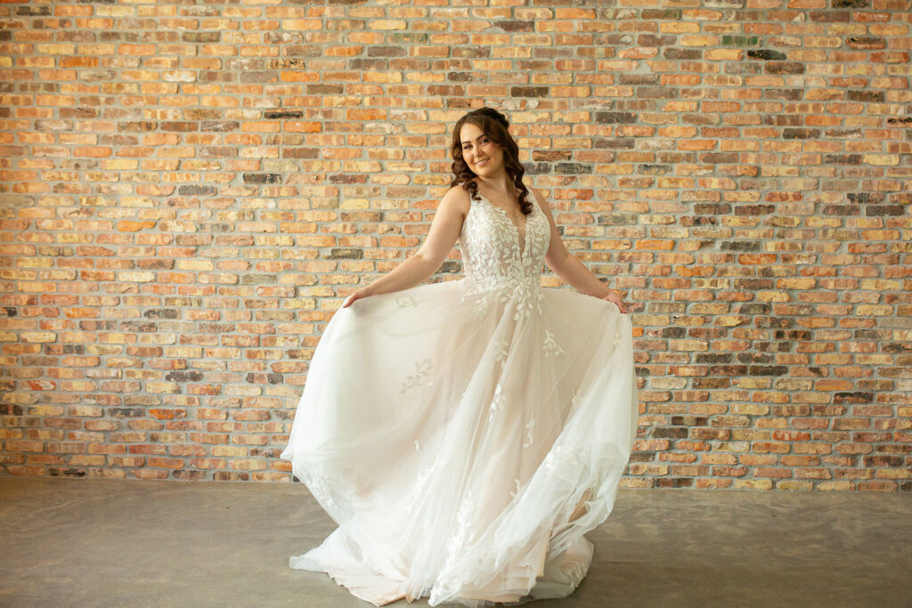 A bride to be modeling the Willow, an A line dress with a V neck, tulle skirt, and leaf applique on the bodice.