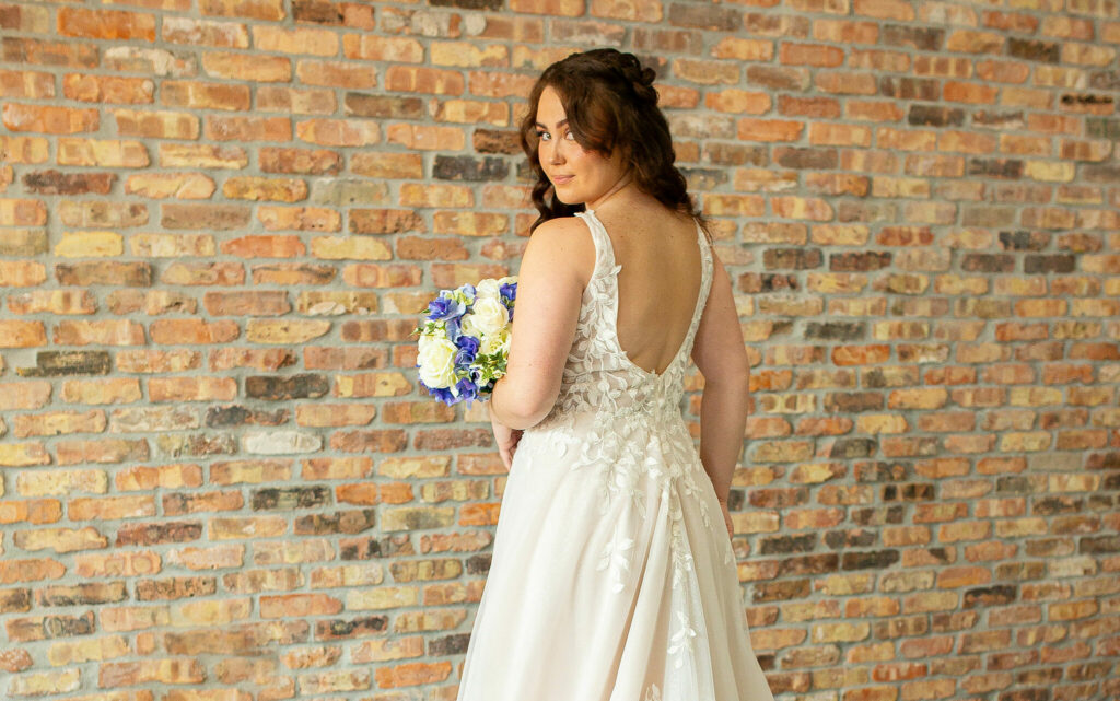 A bride to be modeling the Willow, an A line dress with a V neck, tulle skirt, and leaf applique on the bodice.