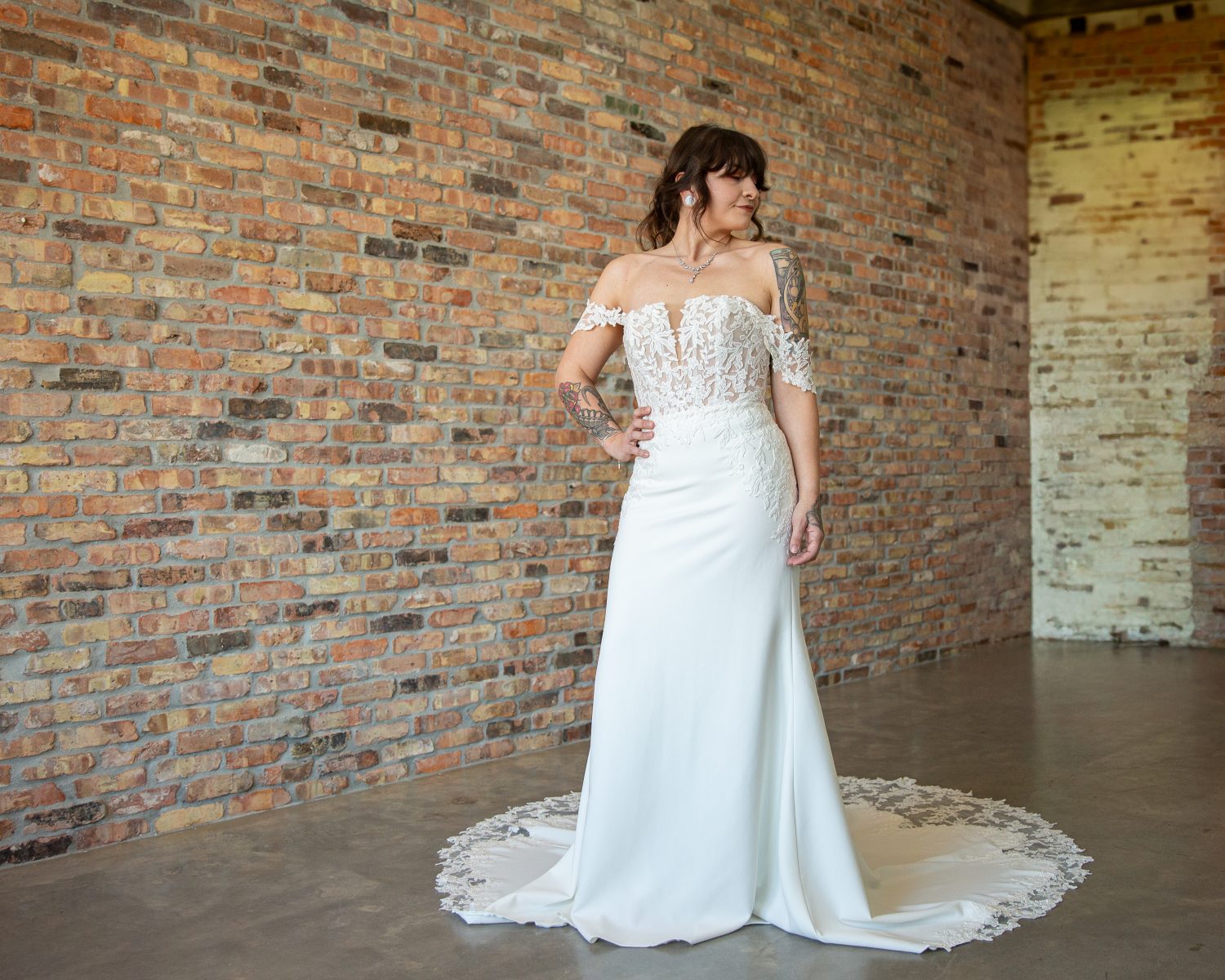 Tattooed bride in Carmen wedding dress, ivory crepe fit-and-flare with notch neckline, detachable straps, sheer bodice, chapel train, front view at Satin and Lace Bridal Boutique, Tampa, FL.