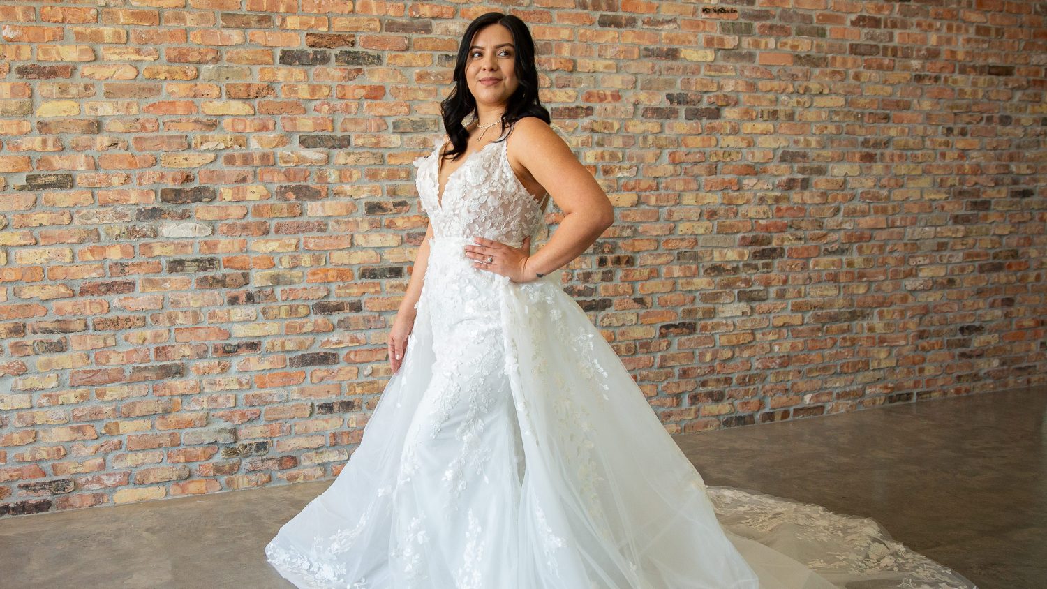 Hispanic bride wearing a fit-and-flare ivory wedding dress with sequined lace, 3D flowers, pearl accents, chapel train, and detachable skirt, full front view at Satin and Lace Bridal Boutique.